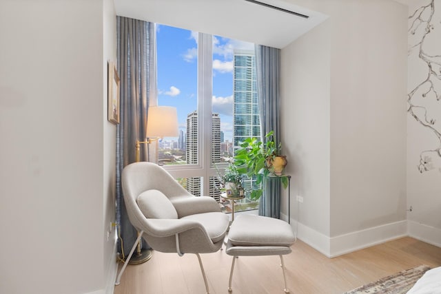 sitting room with a view of city, baseboards, a wall of windows, and wood finished floors