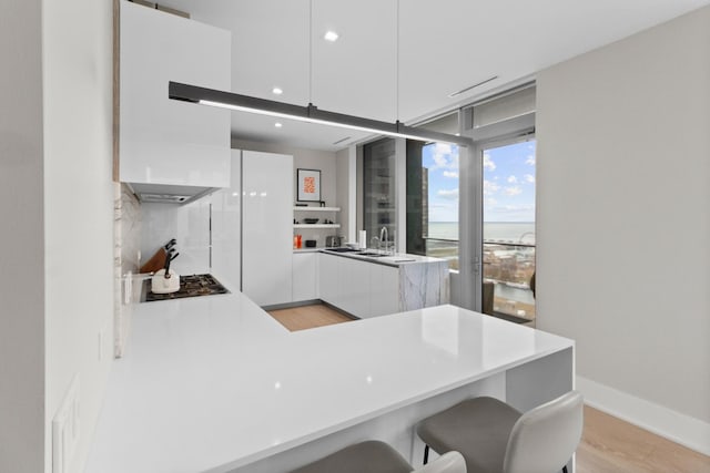 kitchen featuring a peninsula, white cabinetry, light wood-style floors, tasteful backsplash, and modern cabinets