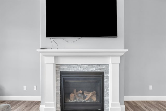 room details with a glass covered fireplace, wood finished floors, and baseboards