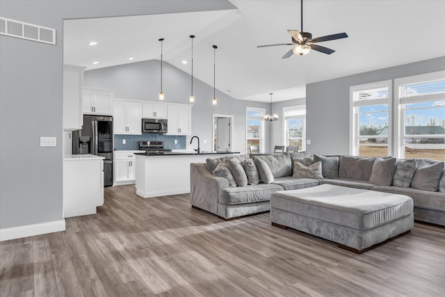 living area featuring visible vents, baseboards, ceiling fan with notable chandelier, wood finished floors, and high vaulted ceiling