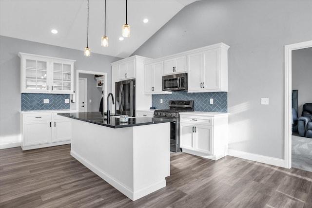 kitchen featuring dark wood-style floors, appliances with stainless steel finishes, glass insert cabinets, and a kitchen island with sink