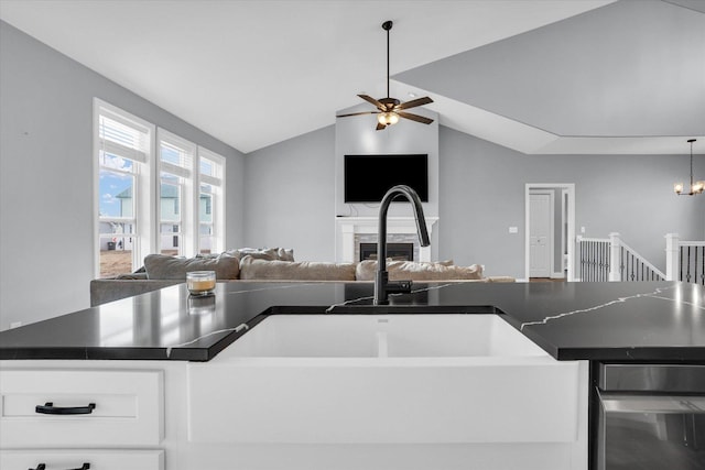 kitchen with lofted ceiling, a fireplace, dark countertops, ceiling fan with notable chandelier, and open floor plan