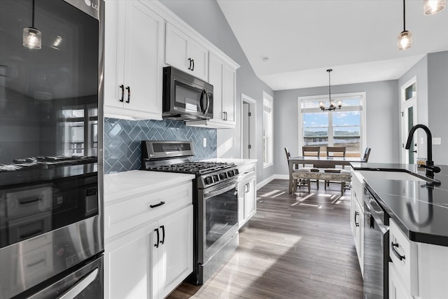 kitchen featuring backsplash, vaulted ceiling, appliances with stainless steel finishes, dark wood-style floors, and a sink