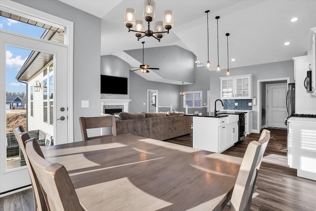 dining room with high vaulted ceiling, ceiling fan with notable chandelier, dark wood finished floors, recessed lighting, and a fireplace