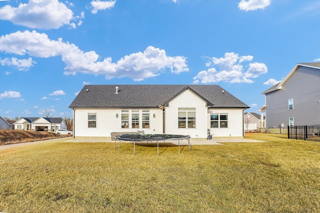 back of house with a shingled roof, a trampoline, fence, a lawn, and a patio