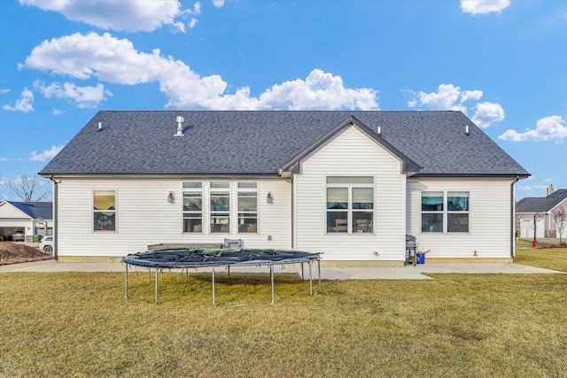 rear view of house featuring a trampoline, roof with shingles, a lawn, and a patio area