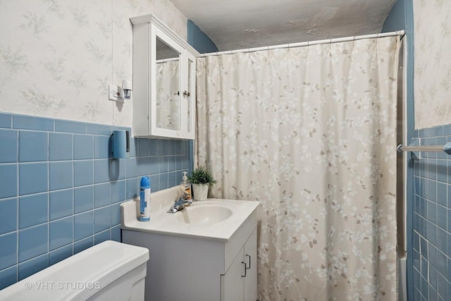 full bath featuring wallpapered walls, toilet, a wainscoted wall, vanity, and tile walls