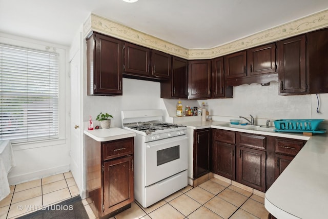 kitchen with light tile patterned flooring, a sink, light countertops, dark brown cabinets, and gas range gas stove