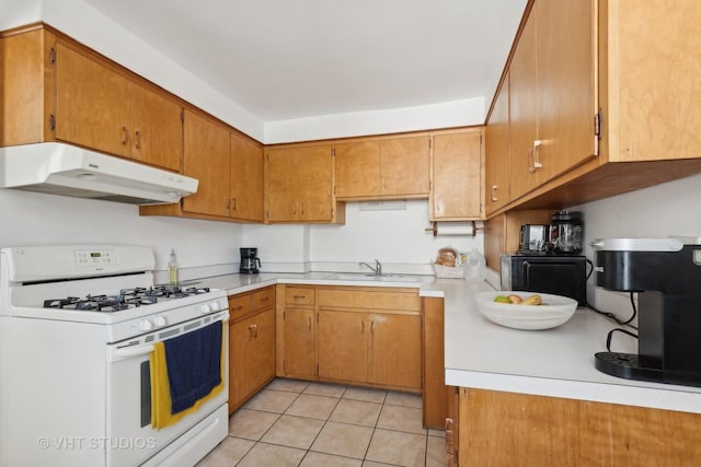 kitchen featuring light tile patterned floors, under cabinet range hood, light countertops, brown cabinetry, and white gas range