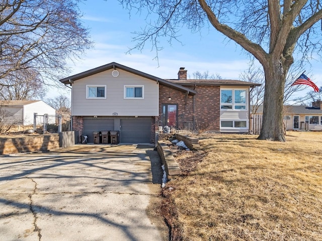 split foyer home with brick siding, a chimney, concrete driveway, an attached garage, and fence