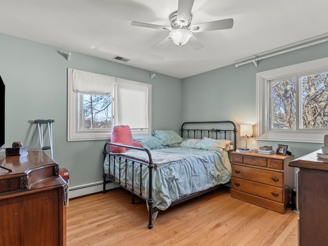 bedroom featuring a baseboard heating unit, multiple windows, and light wood finished floors