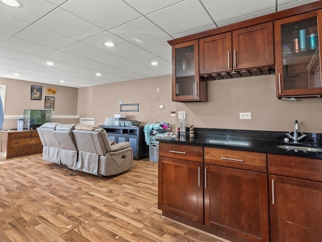 kitchen with dark stone counters, light wood finished floors, a sink, and glass insert cabinets