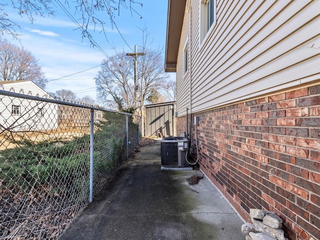 view of side of home with central AC unit, fence, and brick siding