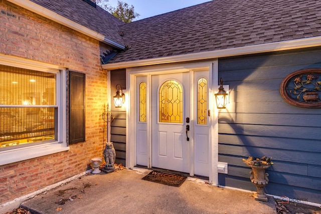 property entrance with a shingled roof and brick siding