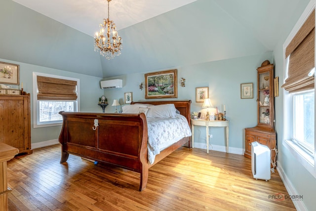 bedroom featuring lofted ceiling, light wood finished floors, multiple windows, and a wall unit AC