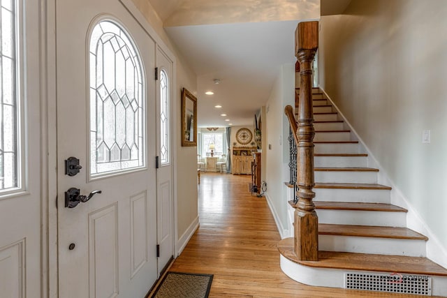 foyer featuring light wood finished floors, baseboards, stairs, a wealth of natural light, and recessed lighting