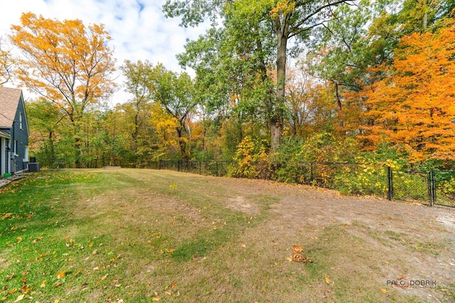 view of yard featuring central AC, fence, and a wooded view