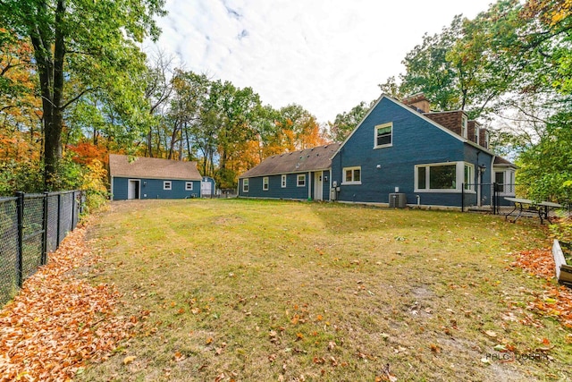 rear view of property with central air condition unit, a fenced backyard, an outdoor structure, and a yard