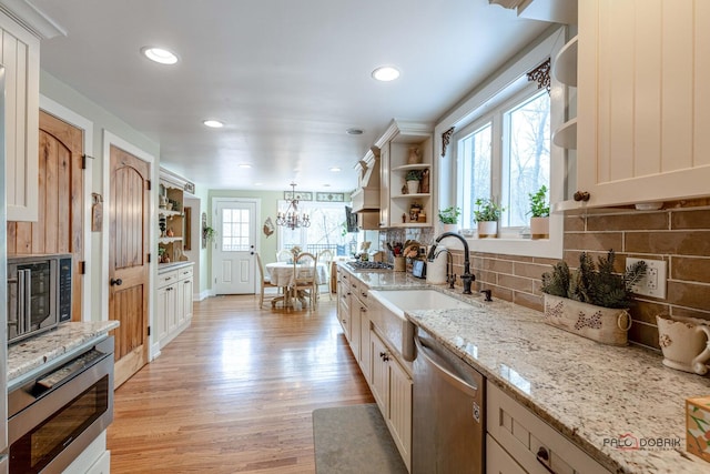 kitchen featuring stainless steel appliances, a sink, light wood finished floors, open shelves, and tasteful backsplash