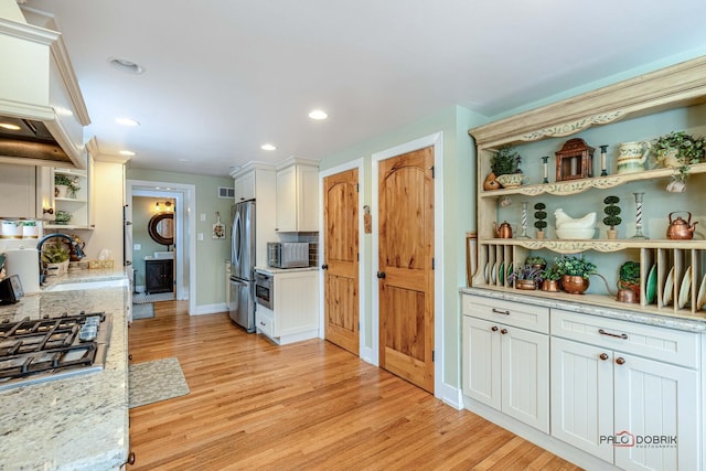 kitchen featuring stainless steel appliances, a sink, light wood-style floors, white cabinets, and open shelves