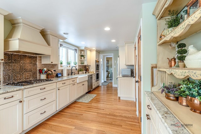 kitchen featuring open shelves, stainless steel appliances, custom range hood, a sink, and light wood-type flooring