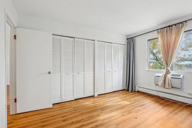 unfurnished bedroom featuring light wood finished floors, a baseboard radiator, and two closets