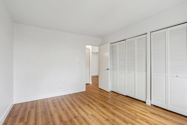 unfurnished bedroom featuring multiple closets, light wood-style flooring, and baseboards