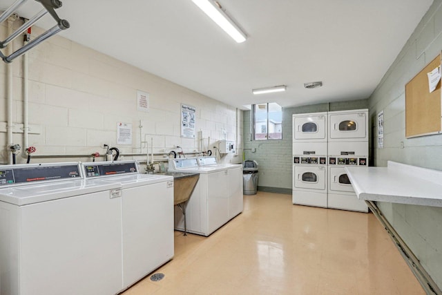 community laundry room with a sink, light floors, stacked washer / drying machine, and washing machine and clothes dryer