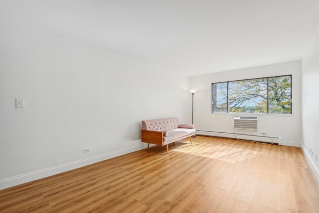 unfurnished room with a baseboard heating unit, a wall unit AC, light wood-style flooring, and baseboards