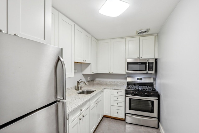 kitchen featuring appliances with stainless steel finishes, white cabinets, a sink, and light tile patterned flooring