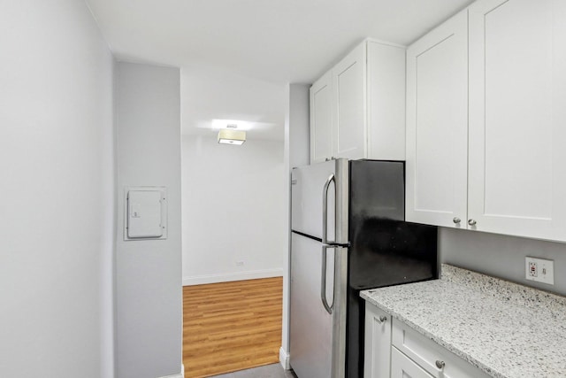 kitchen with light wood-style floors, freestanding refrigerator, white cabinets, light stone countertops, and baseboards