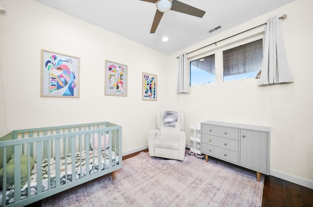 bedroom featuring a crib, baseboards, visible vents, and wood finished floors