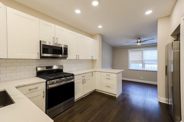 kitchen with light stone counters, dark wood-style flooring, backsplash, appliances with stainless steel finishes, and a peninsula