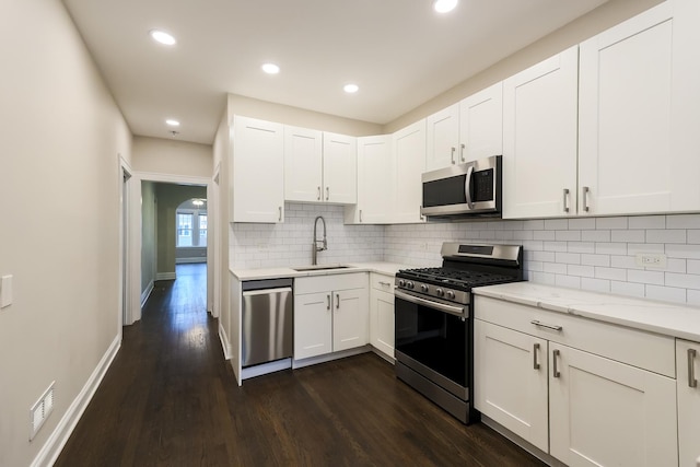 kitchen with appliances with stainless steel finishes, dark wood-style flooring, a sink, and backsplash