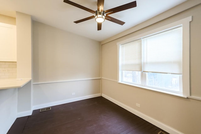 unfurnished room featuring a ceiling fan, dark wood-style flooring, visible vents, and baseboards