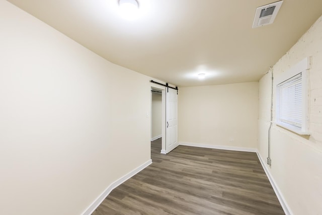 spare room with baseboards, a barn door, visible vents, and wood finished floors