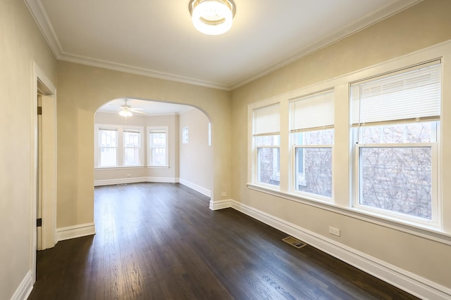 empty room featuring visible vents, arched walkways, dark wood finished floors, baseboards, and ornamental molding