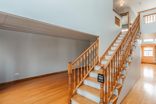 stairway featuring a high ceiling, baseboards, and wood finished floors