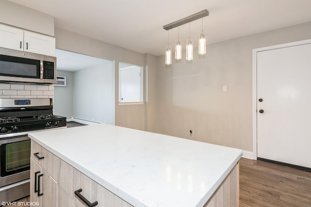 kitchen featuring a center island, pendant lighting, light wood finished floors, stainless steel appliances, and decorative backsplash