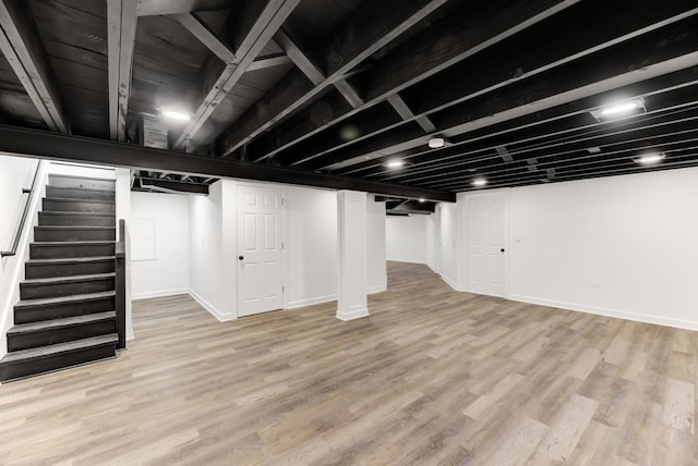 finished basement with baseboards, stairway, and light wood-style floors