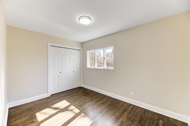 unfurnished bedroom featuring dark wood-style floors, a closet, and baseboards