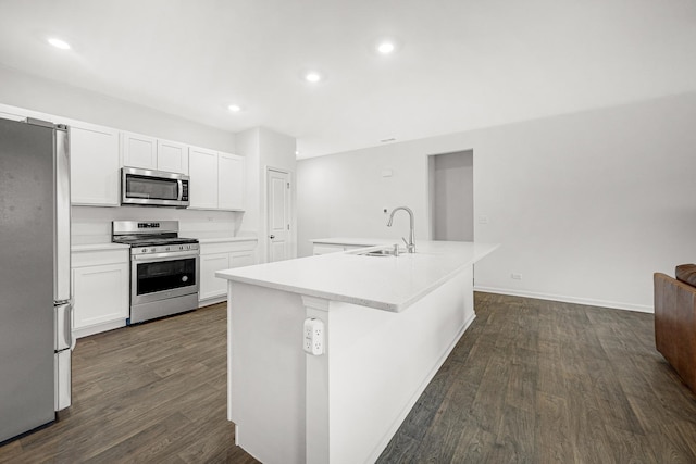 kitchen featuring a kitchen island with sink, stainless steel appliances, dark wood-style flooring, a sink, and light countertops