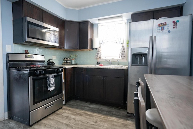 kitchen with stainless steel appliances, a sink, ornamental molding, light wood-type flooring, and backsplash