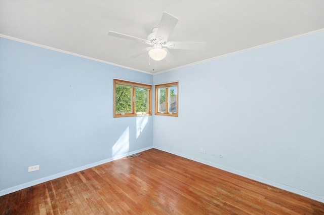 empty room with ornamental molding, wood finished floors, visible vents, and baseboards