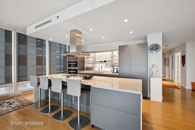 kitchen with island range hood, visible vents, light wood-style floors, a large island, and light stone countertops