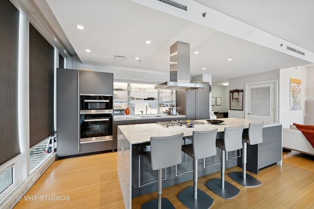 kitchen featuring light wood finished floors, visible vents, modern cabinets, island exhaust hood, and stainless steel appliances