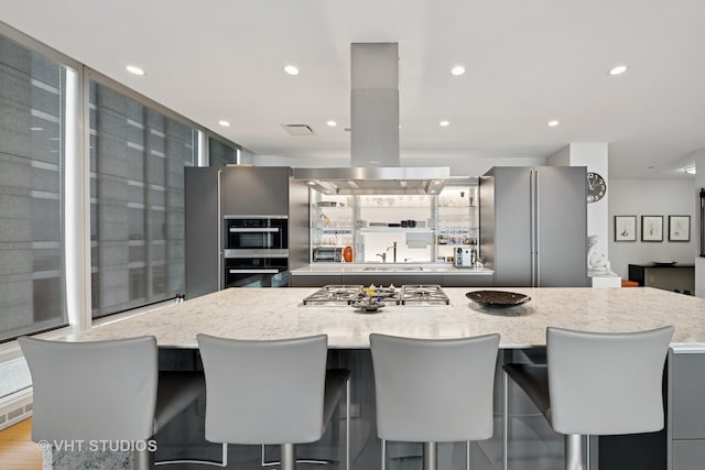 kitchen featuring a spacious island, island exhaust hood, appliances with stainless steel finishes, and light stone counters