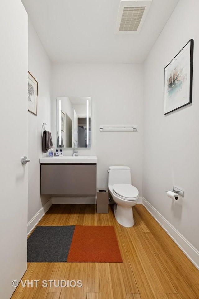 half bath featuring toilet, wood finished floors, vanity, visible vents, and baseboards