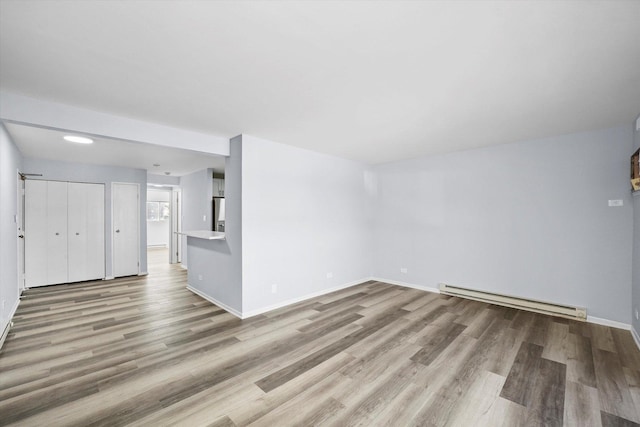 unfurnished living room featuring baseboards, baseboard heating, and wood finished floors