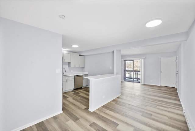 kitchen featuring baseboards, open floor plan, light countertops, stainless steel dishwasher, and light wood-style floors